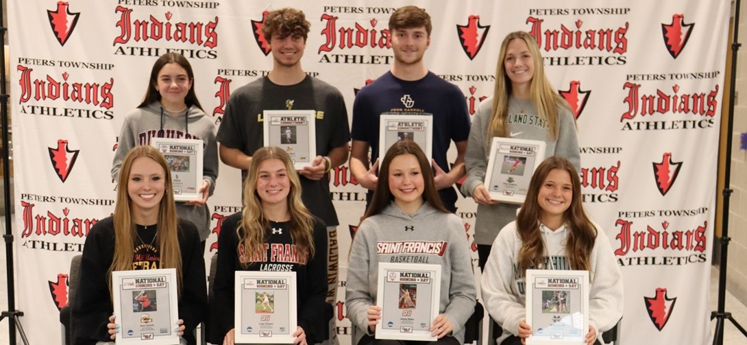 Student athletes pose in front of athletic sign.