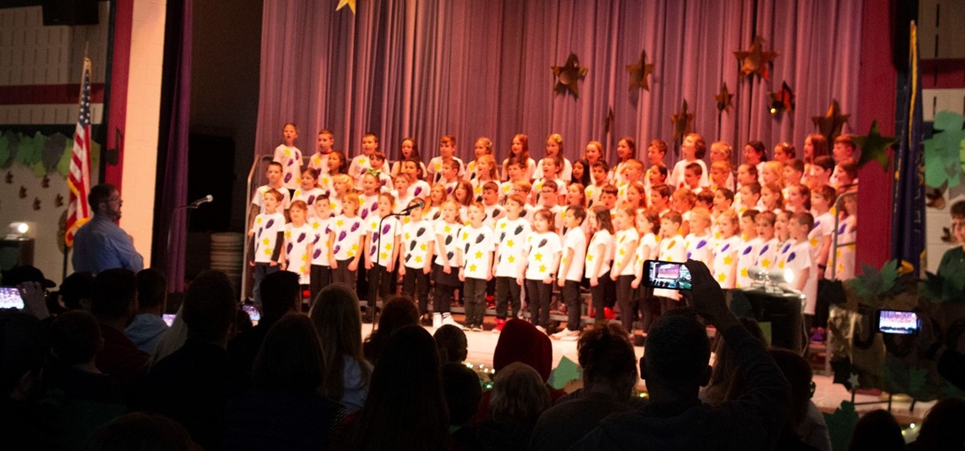 Students on stage singing and wearing dinostaur shirts