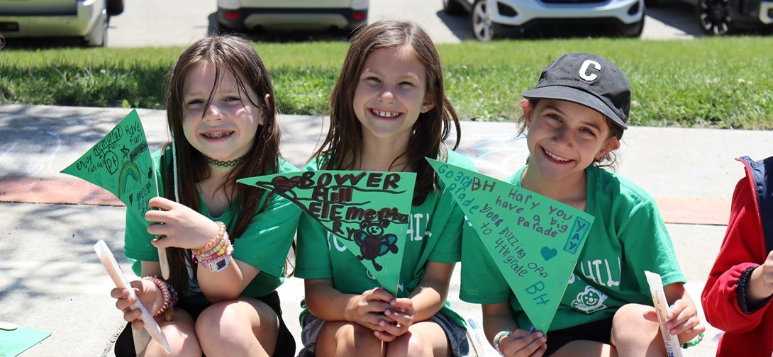 Three girls in green shirts holding flags that say Bower Hill