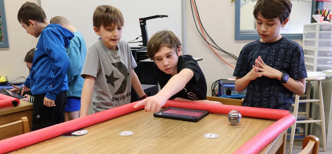 Students hold the ipad to adjust the coding for the round robots.