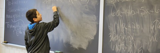 Student at the chalk board doing a math problem.